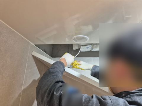 욕실 천장 점검구 판을 내리고 안쪽 배관 쪽으로 손을 넣은 작업자