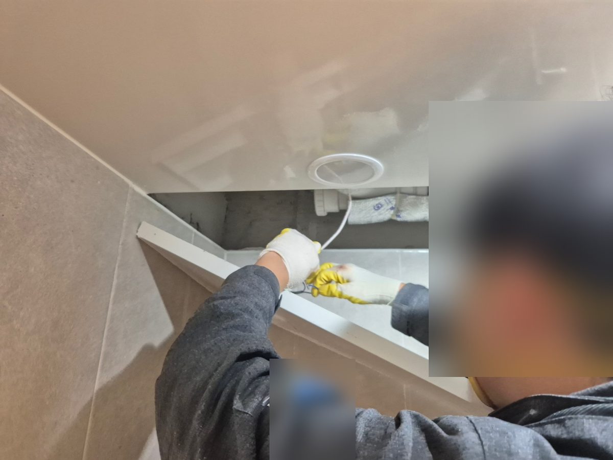 욕실 천장 점검구 판을 내리고 안쪽 배관 쪽으로 손을 넣은 작업자