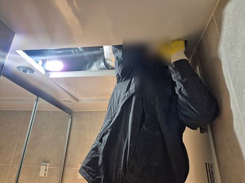 욕실 천장 점검구 안으로 조명을 비추며 두 손을 넣은 작업자