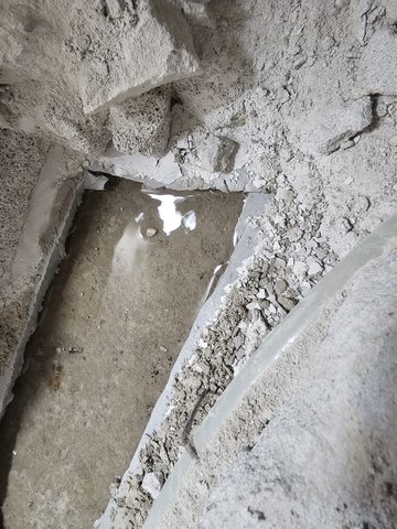 시멘트 바닥을 깨 낸 홈 바닥에 물이 고여 빛을 반사하고 있는 모습