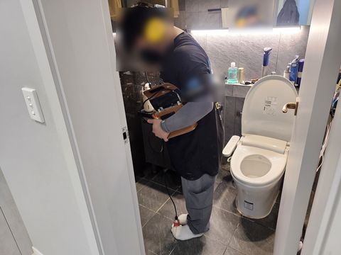 귀덮개를 쓰고 청음 장비 본체를 든 채 욕실 문 앞에 선 작업자