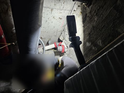 조명을 세워 둔 좁은 천장 속에서 장갑 낀 손으로 흰 관 이음부를 다루는 작업자