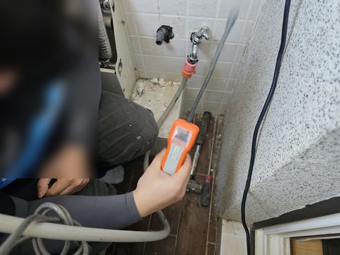 수전 아래 바닥에 주황색 측정 장비를 대 보는 작업자 손