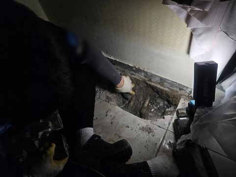 깨어 낸 바닥 가장자리 흙 속에 드러난 녹슨 관 두 줄과 장갑 낀 손