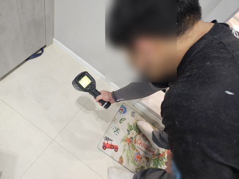 매트가 깔린 타일 바닥에 열화상 카메라를 비추는 작업자