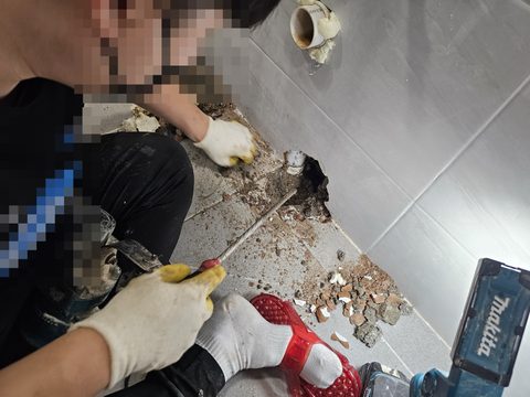 작업자가 타일 벽 아래 모서리 바닥을 정으로 깨 내고 있는 모습