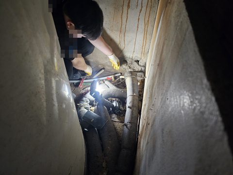 벽 사이 좁은 틈 안에서 조명을 켜 두고 보온재 감은 배관을 살피는 작업자