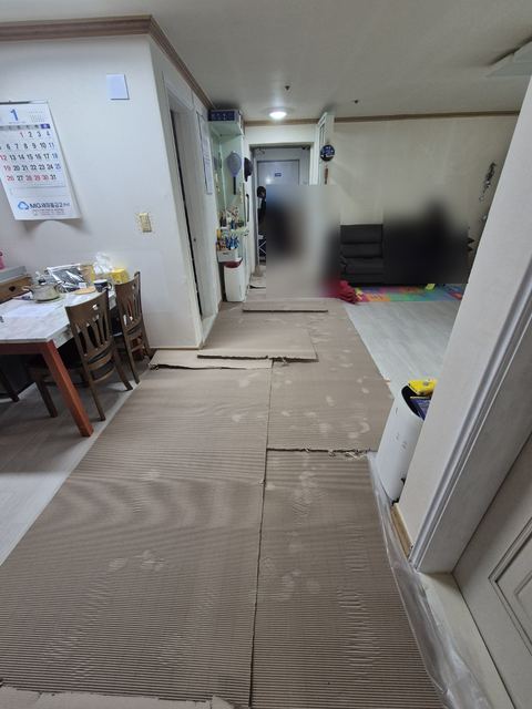 거실 바닥에 보호 판지를 길게 깔아 둔 집 안 복도