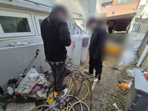 주택 옆 마당에서 호스와 장비를 펼쳐 놓고 선 작업자 두 명