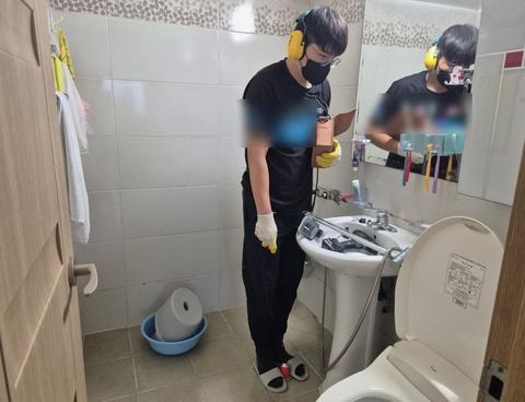 세면대와 변기 사이 바닥을 내려다보며 장비를 든 모습