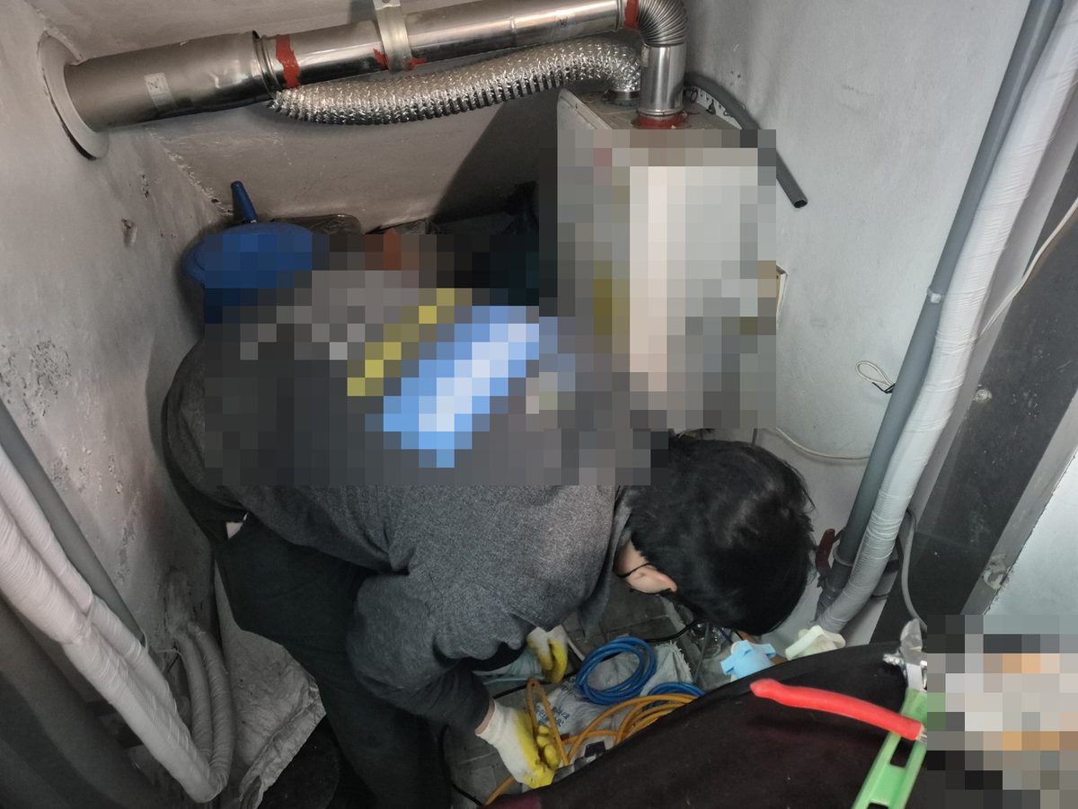 보일러가 달린 좁은 공간에서 몸을 숙여 바닥 쪽 배관을 살피는 작업자