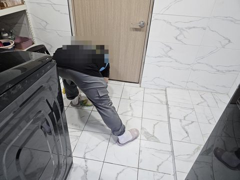 작업자가 허리를 숙여 세탁기 옆 흰 타일 바닥을 걸레로 닦는 모습