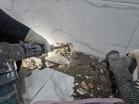 벽과 바닥 경계를 깨낸 자리의 흰 배관·밸브와 쌓인 타일 잔해