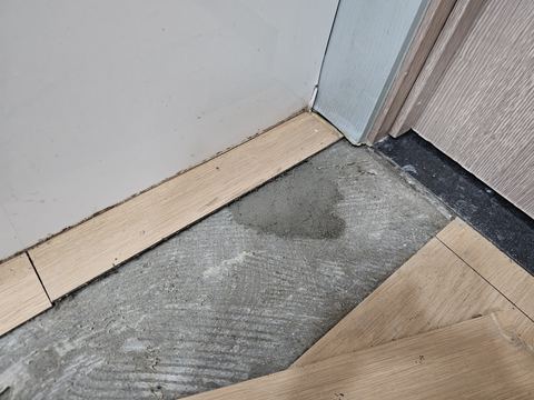 문틀 모서리 마루재를 걷어 낸 시멘트 바닥의 짙은 젖은 얼룩