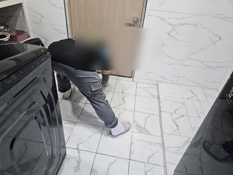 세탁기 사이 흰 타일 바닥에 허리를 숙이고 스펀지질하는 작업자