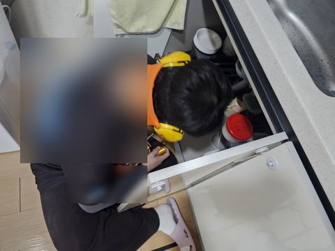 하부장 문을 연 싱크대 앞에서 헤드폰을 쓰고 청음 장비를 다루는 뒷모습