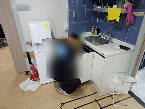 검은 테이프 선이 붙은 바닥에 앉아 하부장 속 소리를 듣는 작업자