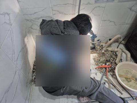 깨낸 타일 잔해와 파이프 커터·플라이어·대야 곁에서 몸을 숙인 작업자