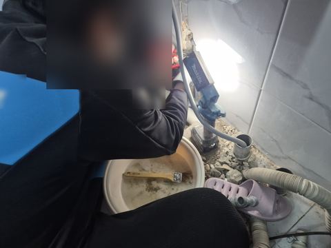 작업등 불빛 아래 벽 밑 배관을 플라이어로 집은 손과 탁한 물 담긴 대야