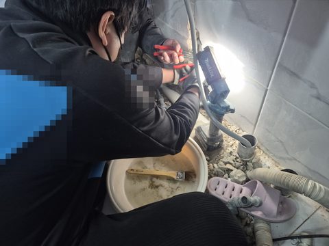 조명을 비춘 벽 아래 배관 쪽으로 몸을 숙여 공구를 쓰는 작업자