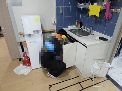 헤드폰을 쓴 작업자가 주방 싱크대 하부장 문을 열고 안쪽을 살피는 모습
