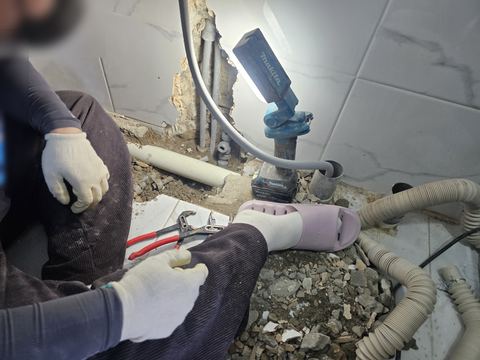 부분 철거한 타일 벽 밑 세로·바닥 배관을 비추는 작업등과 타일 조각 더미