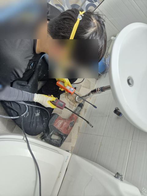 세면대 배수관 곁 바닥에 탐지기 센서를 붙이고 화면을 보는 작업자