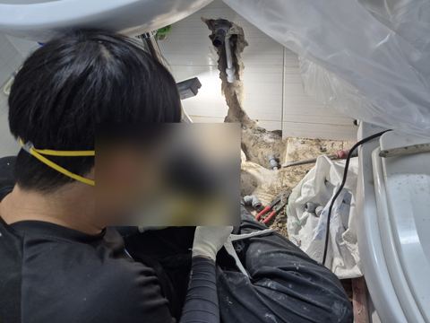 따낸 벽 홈 앞에서 작은 공구로 배관 끝을 다듬는 작업자