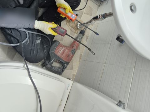 변기와 세면대 사이 바닥에서 측정 기기 두 대를 양손에 쥔 모습