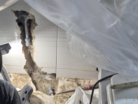 비닐로 덮은 세면대 아래로 이어진 벽 개방 자리와 깨어 낸 바닥